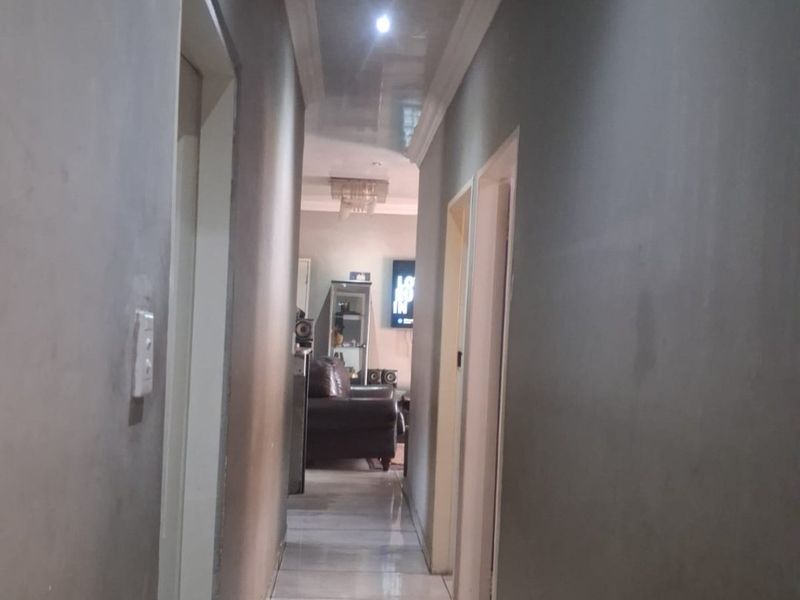 A narrow hallway featuring tiled flooring, recessed downlighting, and a coved ceiling, leading towards the main living area.