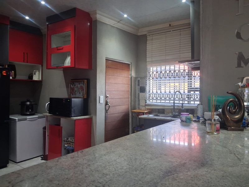 Kitchen featuring granite countertops, red cabinetry, and a stainless steel sink, with a security gate on the window and recessed lighting.