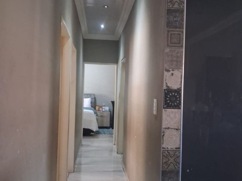 A well-lit hallway featuring tiled flooring, decorative tile accents, and a modern recessed ceiling design, providing access to adjacent rooms.