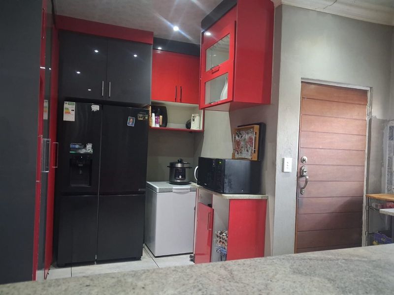 Kitchen area featuring high-gloss red and black cabinetry, stone countertops, and recessed lighting, with a solid wood door leading to the exterior.