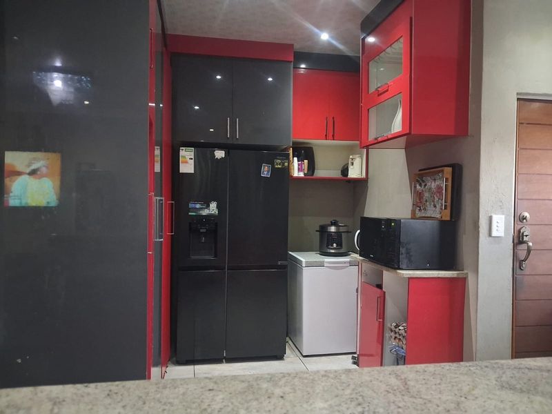 A compact kitchen area featuring high-gloss red and black cabinetry, granite countertops, and integrated storage space.