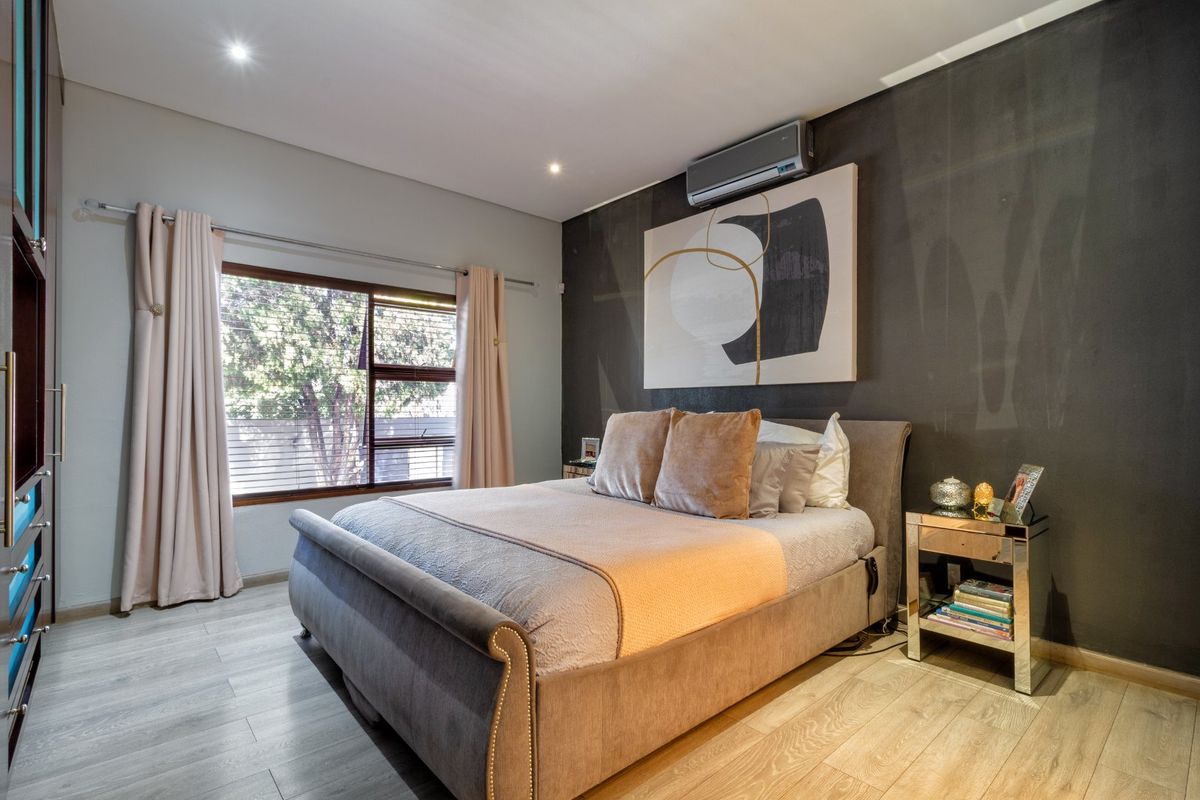 A well-maintained bedroom featuring modern laminate flooring, built-in cupboards, recessed lighting, and a wall-mounted air conditioning unit.