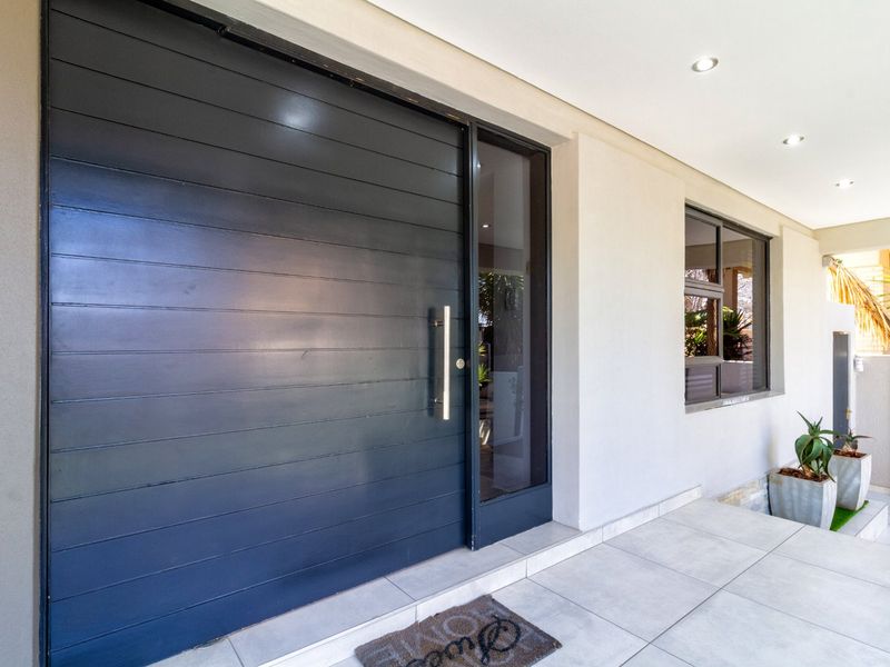 Modern front entrance featuring a large dark horizontal-slatted pivot door with a glass sidelight and clean tiled porch area.