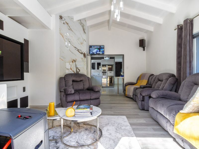 A bright living room featuring a vaulted ceiling with exposed beams, a marble-look feature wall, and modern laminate flooring.