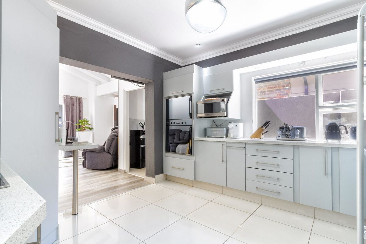 Modern kitchen featuring light-toned cabinetry, stone countertops, built-in oven and microwave, and tiled flooring, with an open-plan flow to the adjacent living area.