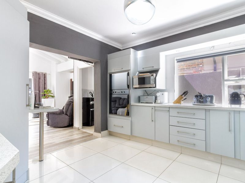 Modern kitchen featuring light-toned cabinetry, stone countertops, built-in oven and microwave, and tiled flooring, with an open-plan flow to the adjacent living area.