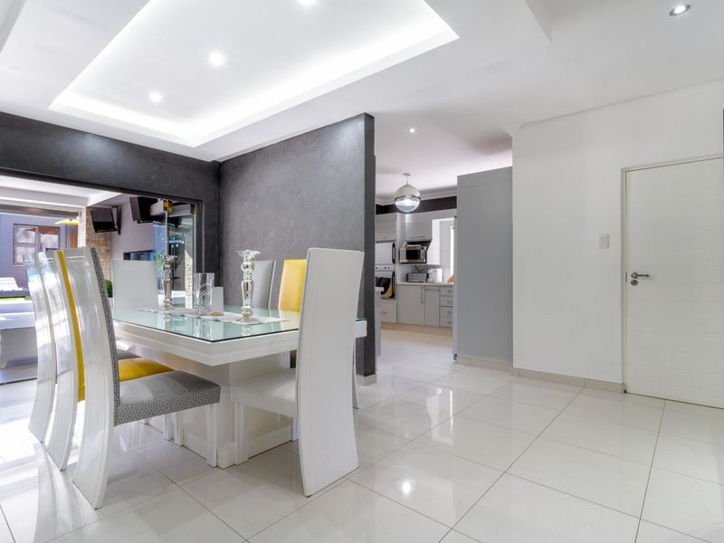 Modern open-plan dining area featuring sleek tiled floors, recessed ceiling lighting, and a seamless transition to the adjacent kitchen and outdoor patio space.