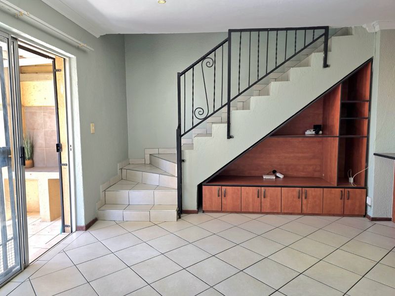 Living area featuring a tiled staircase with wrought iron railing and integrated under-stair storage cabinetry, leading to an outdoor patio area.