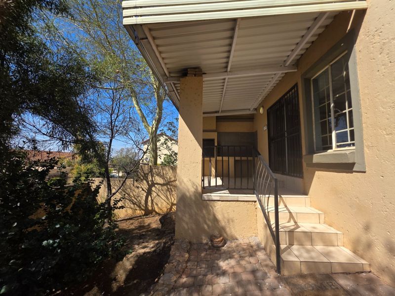 Covered patio area featuring a built-in braai, tiled flooring, and metal security gate, providing a functional outdoor entertainment space.