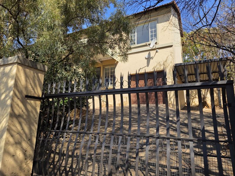 Front exterior view of a two-story townhouse featuring a metal security gate, driveway, and garage access.