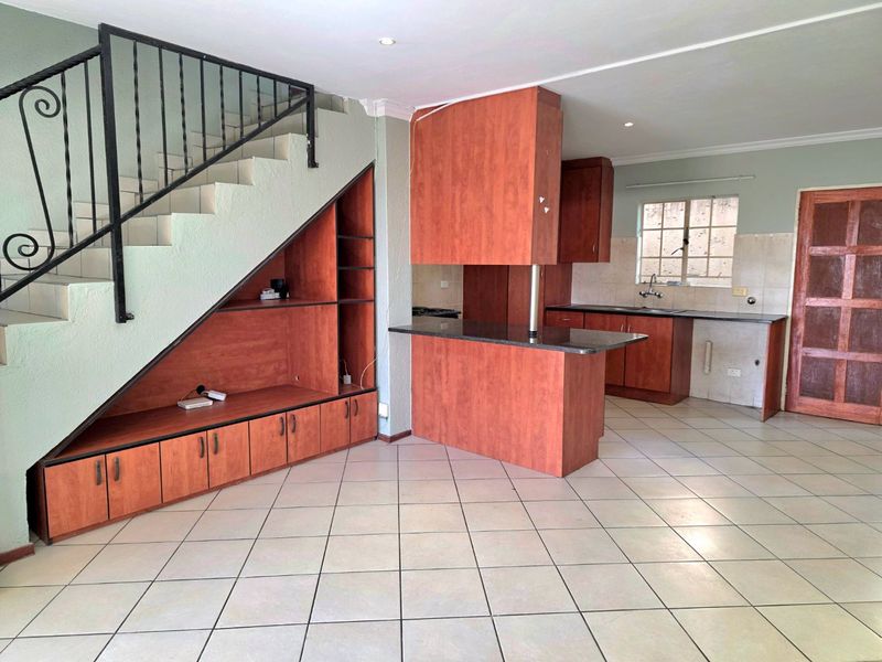 Open plan living and kitchen area featuring built-in cabinetry, granite countertops, ceramic tile flooring, and a staircase with a metal railing.