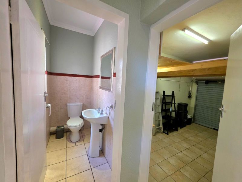 A functional guest bathroom featuring a pedestal basin and toilet, adjacent to a garage space with a mezzanine storage level.
