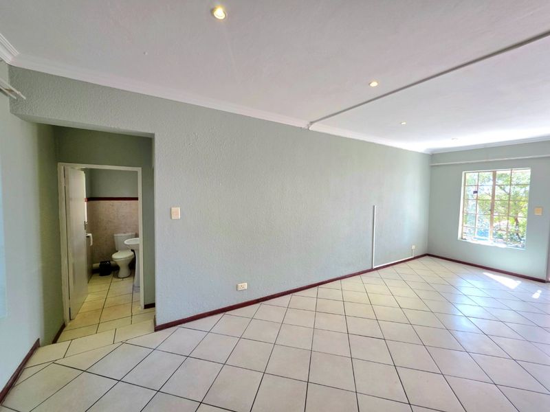 An empty living area featuring tiled flooring, recessed lighting, and a view into an adjacent bathroom, with neutral wall finishes.