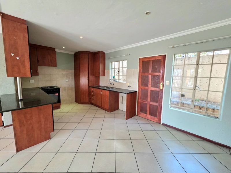 A functional kitchen featuring dark wood cabinetry, granite countertops, tiled flooring, and direct access to the exterior via a wooden door.