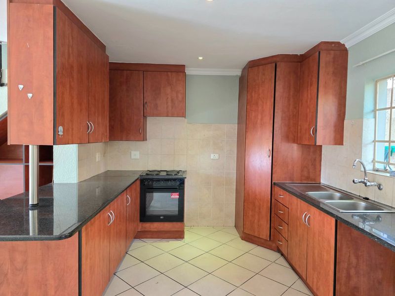 A functional kitchen featuring wooden cabinetry, granite countertops, a built-in electric stove and oven, and a double sink with tiled backsplash.