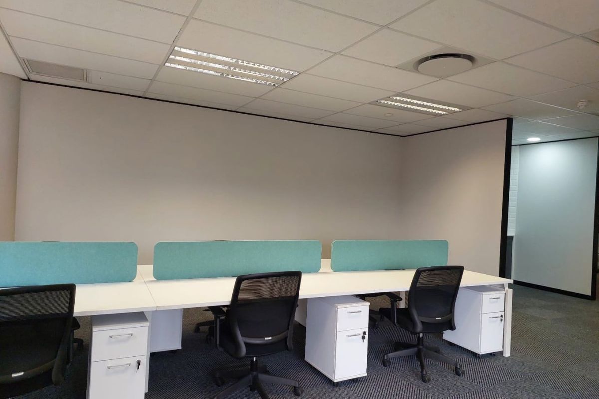 A modern commercial office space featuring a clean, professional layout with built-in desk partitions, suspended ceilings, and durable carpet tile flooring.
