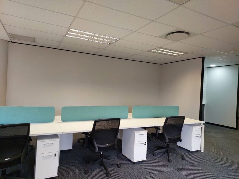 A modern commercial office space featuring a clean, professional layout with built-in desk partitions, suspended ceilings, and durable carpet tile flooring.