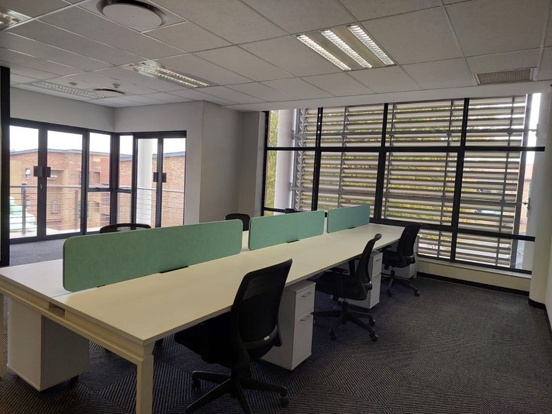 A bright, modern commercial office space featuring a suspended ceiling, large windows with external louvers, and carpeted flooring, suitable for a professional work environment.