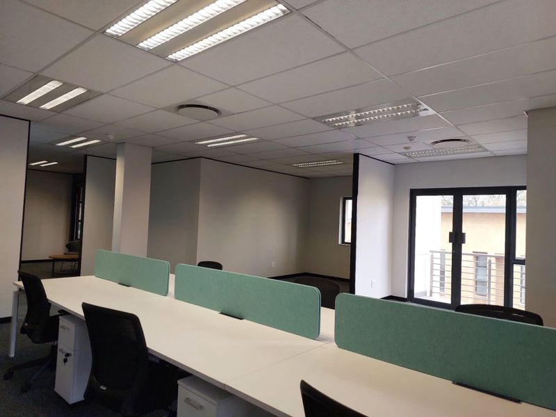 Modern open-plan office space featuring suspended ceilings, recessed lighting, partition dividers, and direct access to an exterior balcony area.