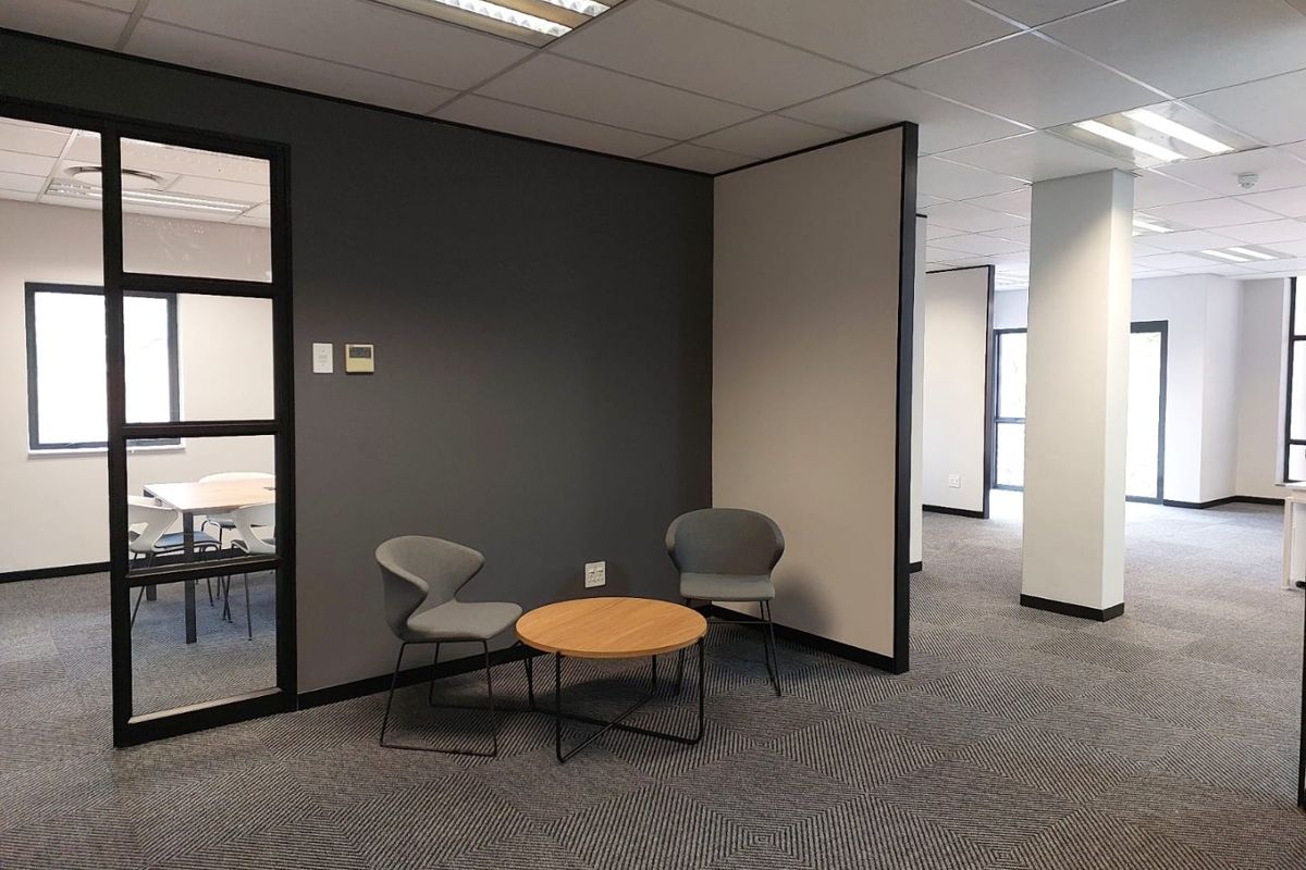 Modern commercial office space featuring carpeted flooring, suspended ceilings with recessed lighting, and partitioned work areas with glass detailing.