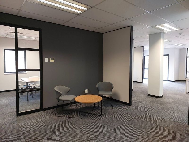 Modern commercial office space featuring carpeted flooring, suspended ceilings with recessed lighting, and partitioned work areas with glass detailing.