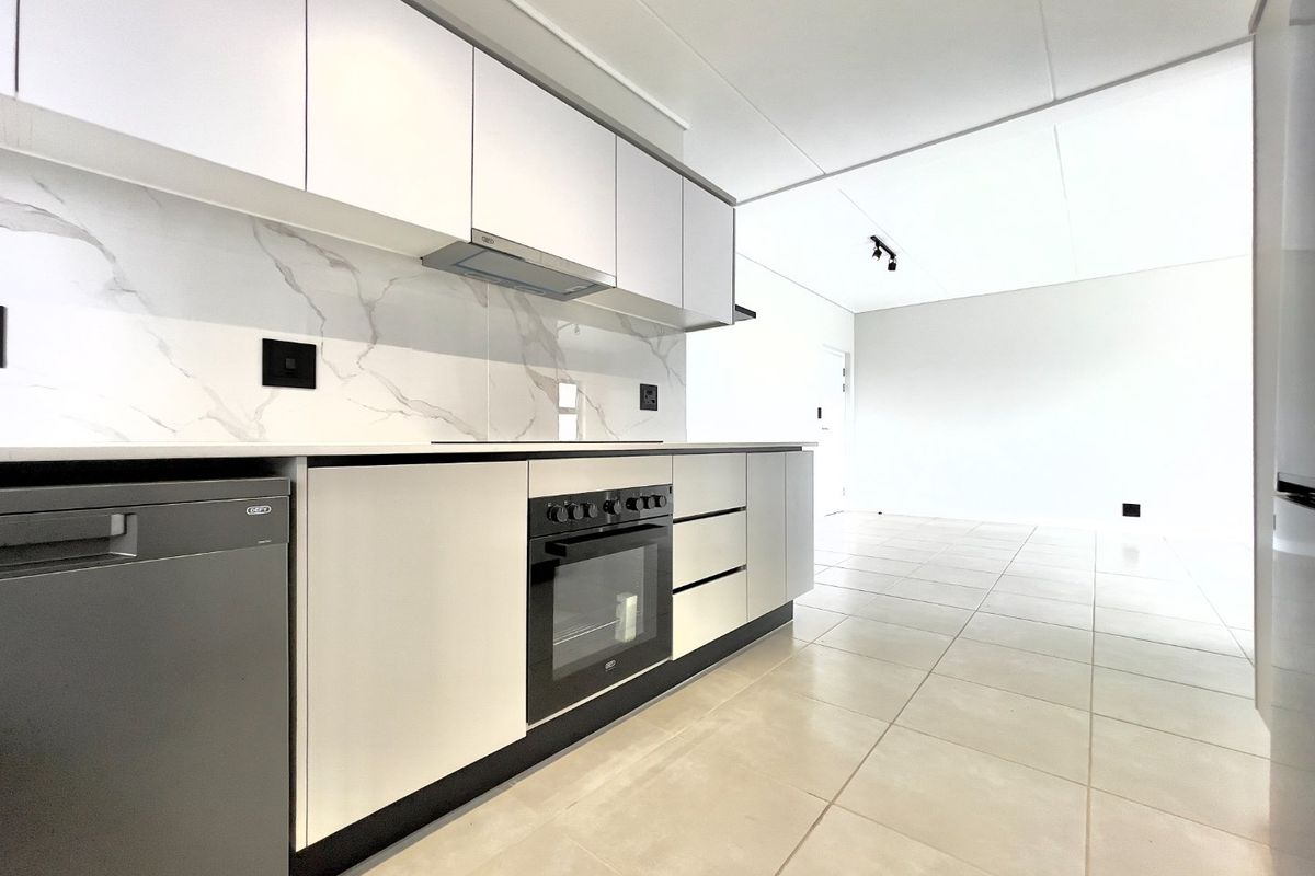 Modern open-plan kitchen featuring sleek white cabinetry, marble-look splashback, integrated oven, and tiled flooring, flowing into a bright, spacious living area.