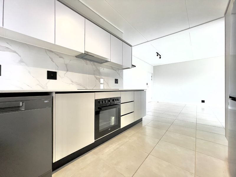Modern open-plan kitchen featuring sleek white cabinetry, marble-look splashback, integrated oven, and tiled flooring, flowing into a bright, spacious living area.