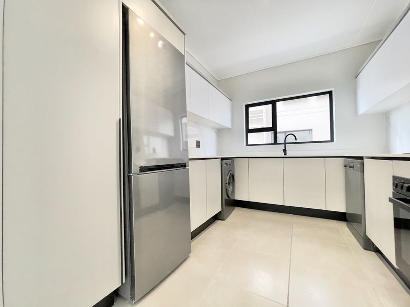 Modern kitchen featuring sleek white cabinetry, stone countertops, integrated appliances, and high-quality tiled flooring with a clean, contemporary aesthetic.