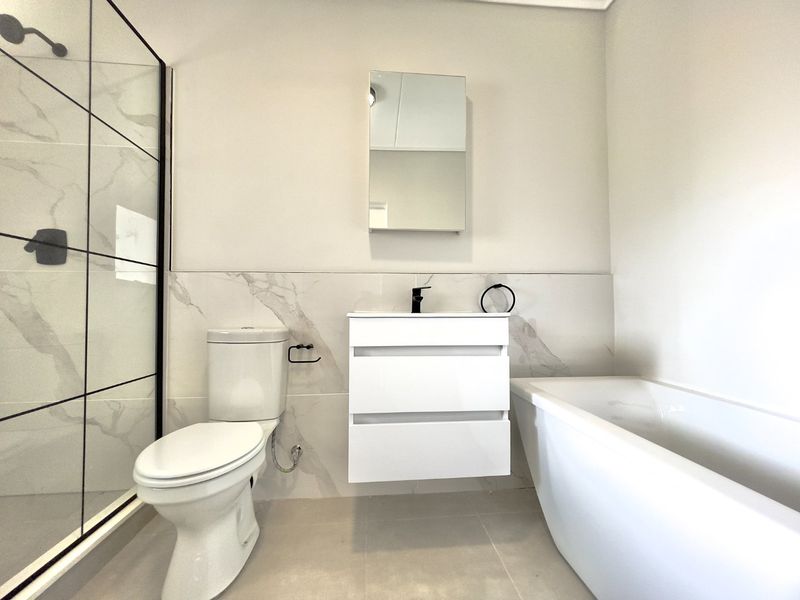 Modern bathroom featuring a walk-in shower with black-framed glass, a sleek wall-mounted vanity, a freestanding bathtub, and elegant marble-look wall tiling.