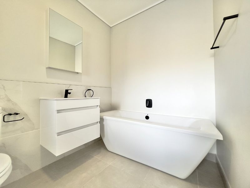 Modern bathroom featuring a sleek freestanding bathtub, wall-mounted vanity with basin, and contemporary matte black fixtures against neutral tiled walls.
