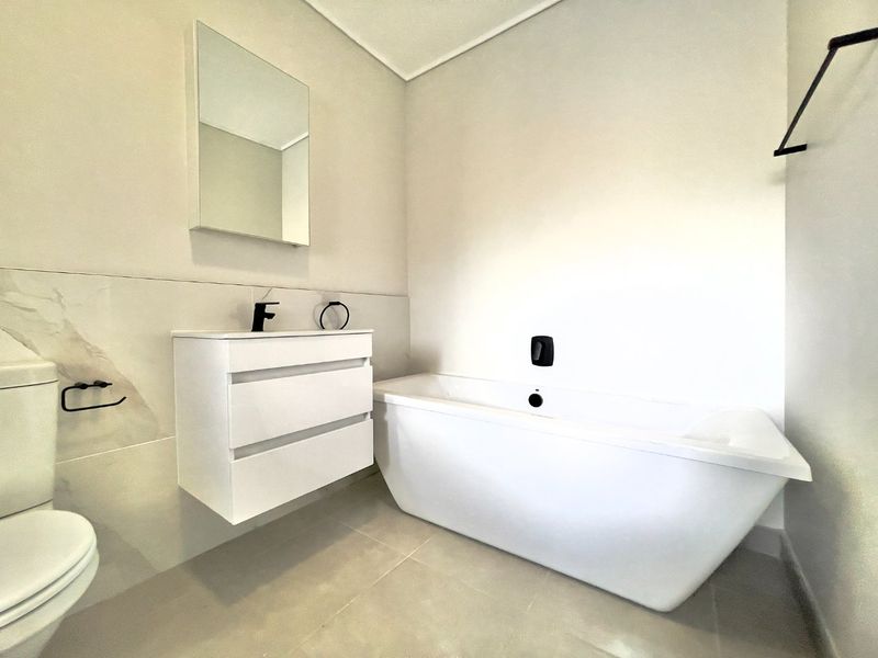 Modern bathroom featuring a sleek freestanding bathtub, wall-mounted vanity with basin, and contemporary black fixtures in a clean, minimalist setting.