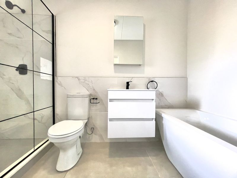 Modern bathroom featuring a walk-in shower with black-framed glass, a wall-mounted vanity, a bathtub, and contemporary marble-look wall tiles.