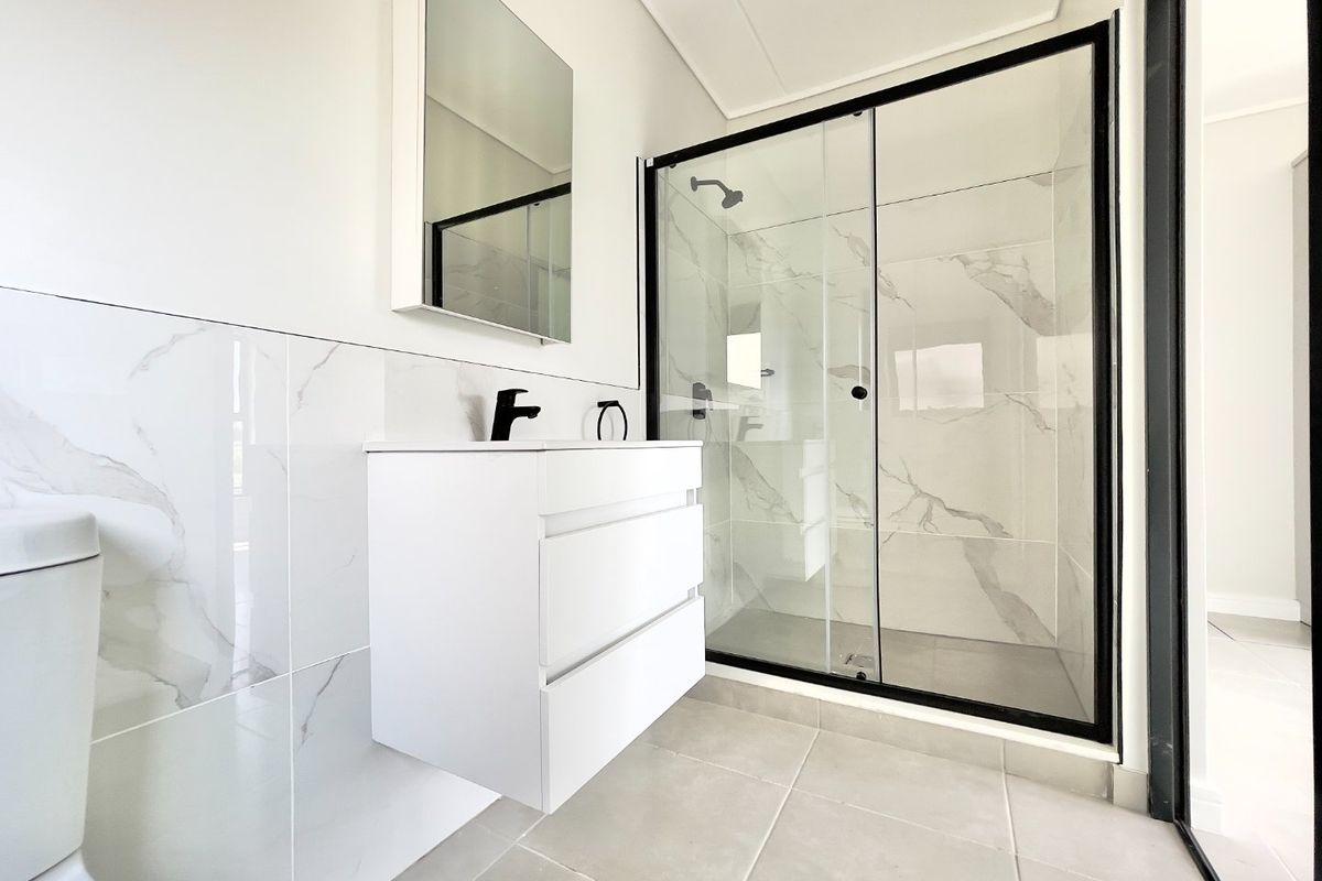 Modern bathroom featuring a wall-mounted vanity, black fixtures, and a spacious glass-enclosed shower with marble-look wall tiling.