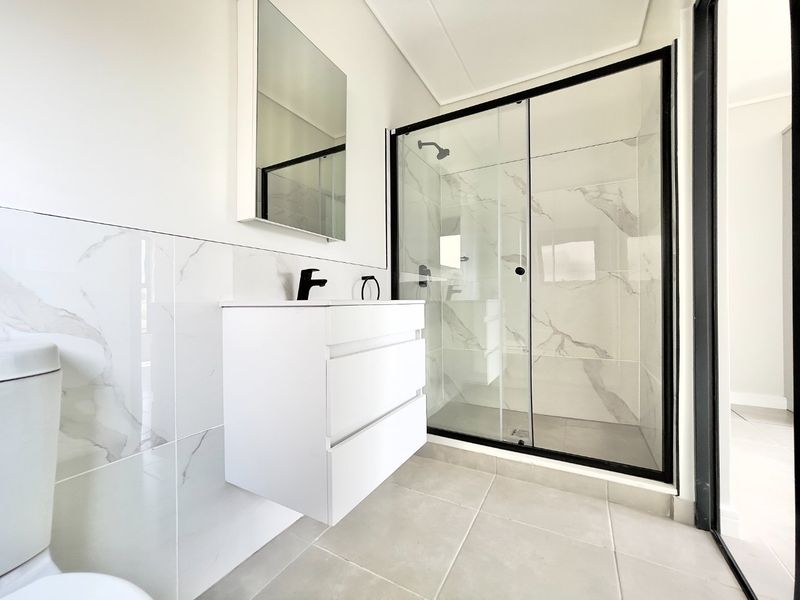 Modern bathroom featuring a wall-mounted vanity, black fixtures, and a spacious glass-enclosed shower with marble-look wall tiling.