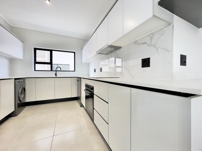Modern kitchen featuring sleek white cabinetry, stone countertops, marble-look splashback, built-in oven, extractor fan, and tiled flooring.