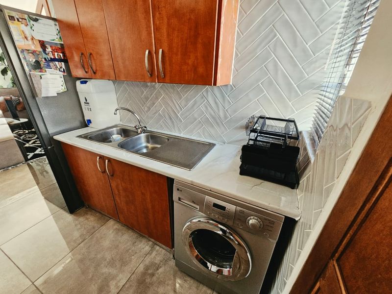 A functional scullery area featuring wood-finish cabinetry, a stainless steel sink, stone countertops, and a stylish herringbone tile backsplash.