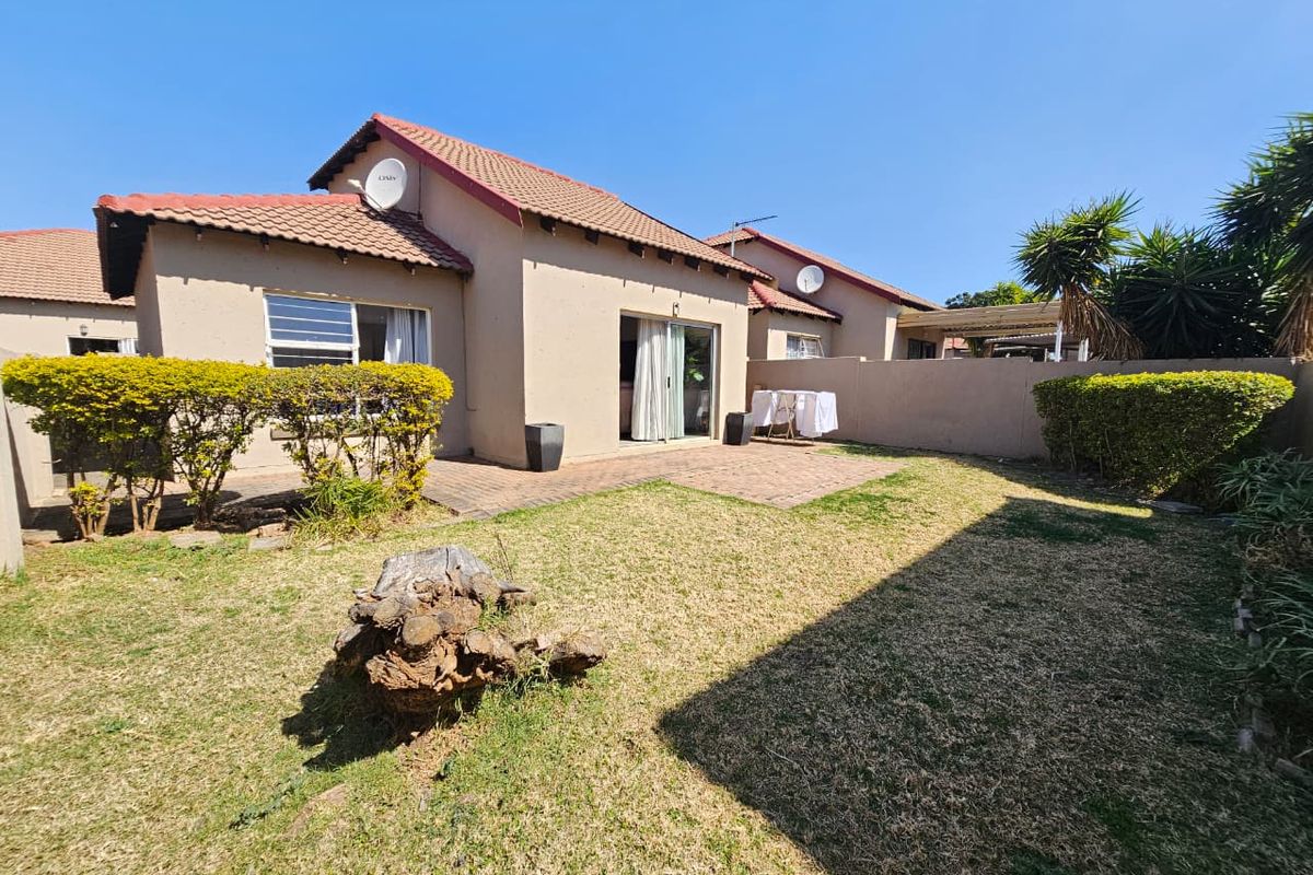 Rear view of the townhouse featuring a paved patio area, private garden space, and a tiled roof structure.