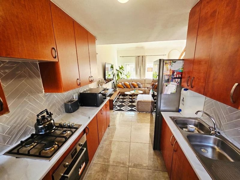 Open-plan kitchen and living area featuring wood-finish cabinetry, gas hob, built-in oven, and tiled flooring throughout the space.