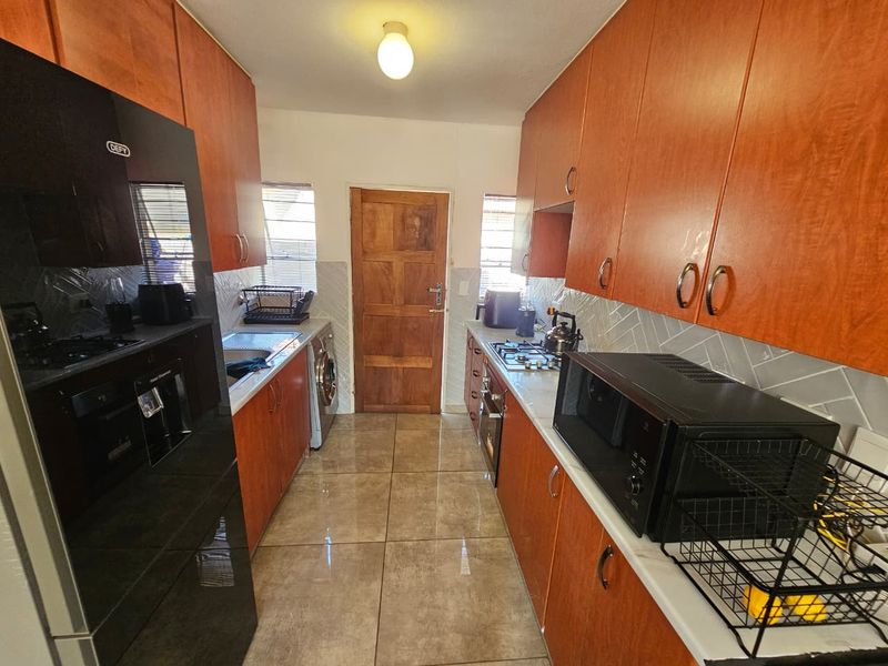 A galley-style kitchen featuring wood-finish cabinetry, tiled flooring, a gas hob, and built-in oven, providing a functional workspace.