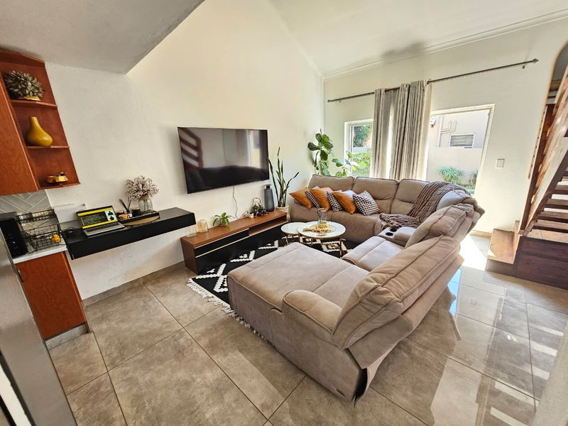 A bright, open-plan living room featuring vaulted ceilings, large format floor tiles, and a staircase leading to an upper level.