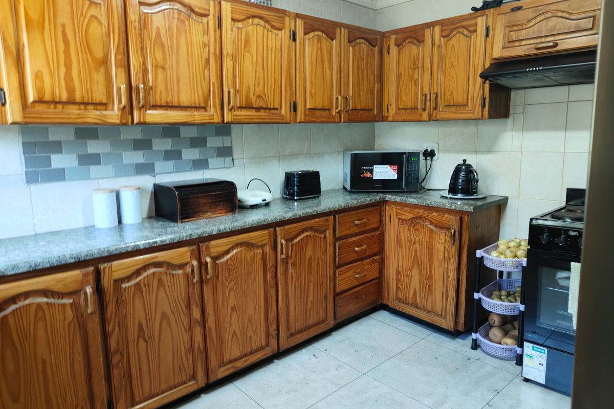 A functional kitchen featuring traditional wooden cabinetry, granite countertops, a tiled backsplash, and a freestanding oven with an integrated extractor fan.