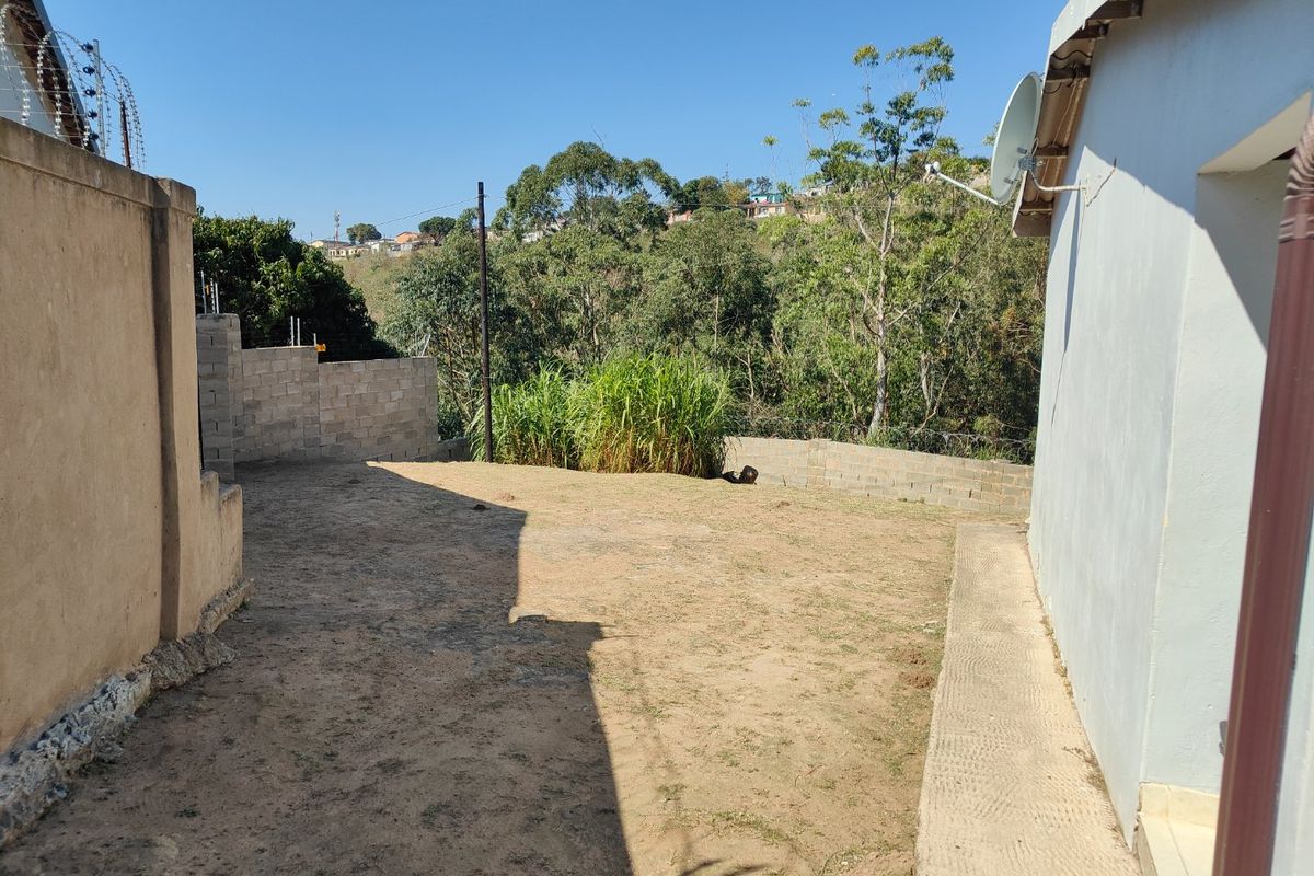 A rear yard area featuring a concrete block boundary wall with razor wire, satellite dish, and an unlandscaped, bare earth ground surface.