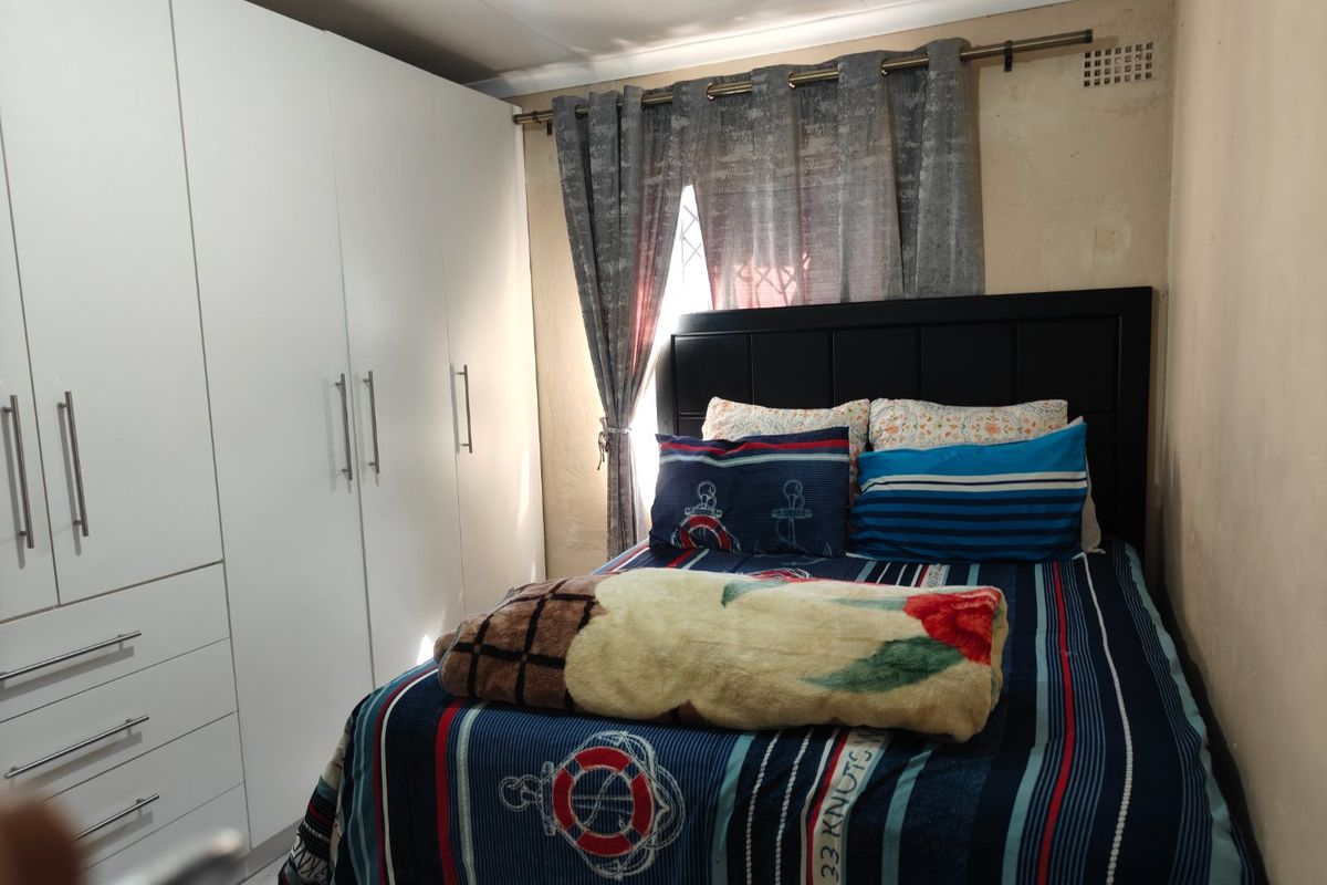 A bedroom featuring white built-in cupboards and a window with a curtain rod, showing signs of wear on the wall surfaces.