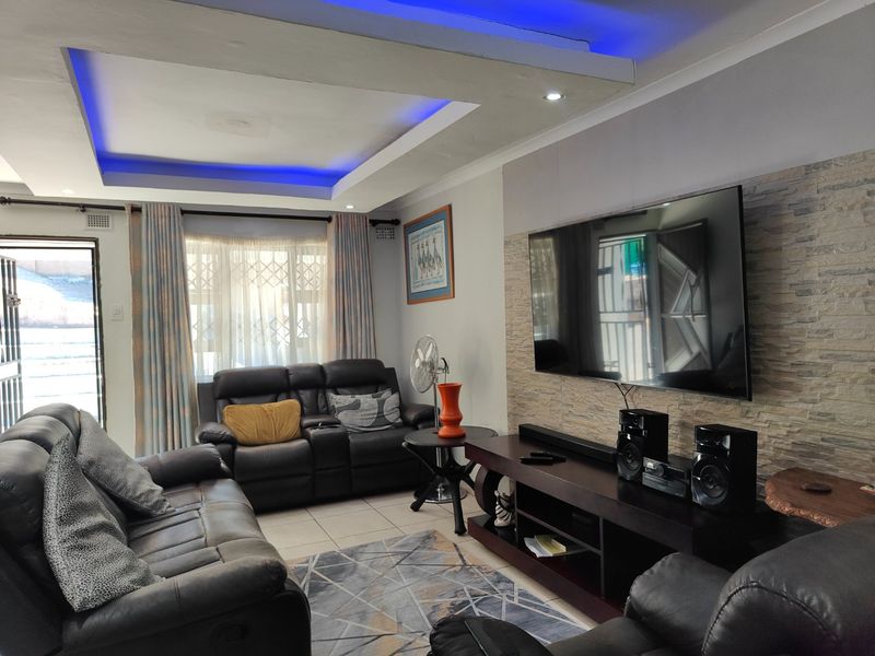 A comfortable living room featuring a stone-clad feature wall, recessed ceiling with blue LED accent lighting, and tiled flooring.