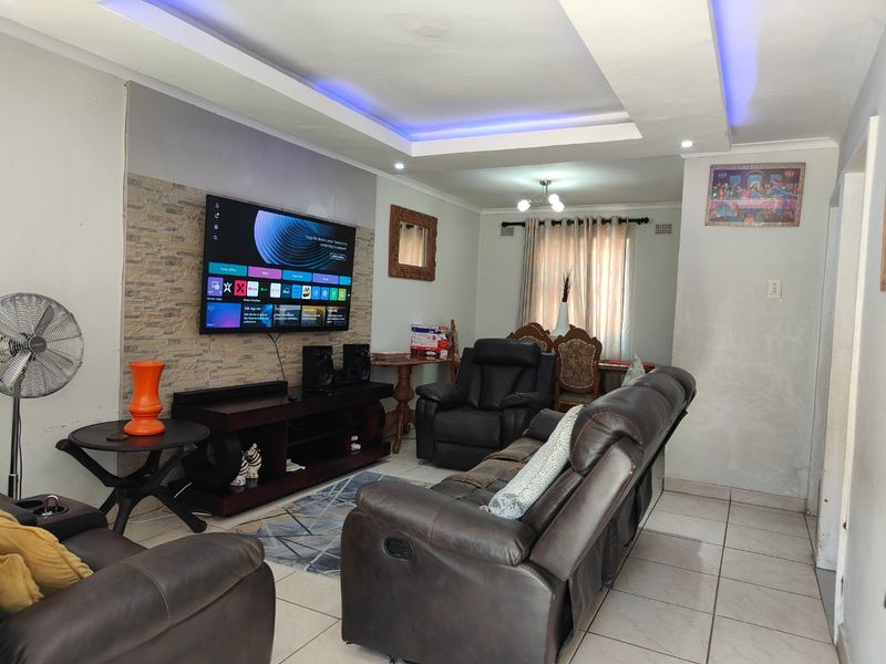 A living room featuring a stone veneer accent wall, recessed ceiling with integrated LED lighting, and neutral ceramic floor tiles.