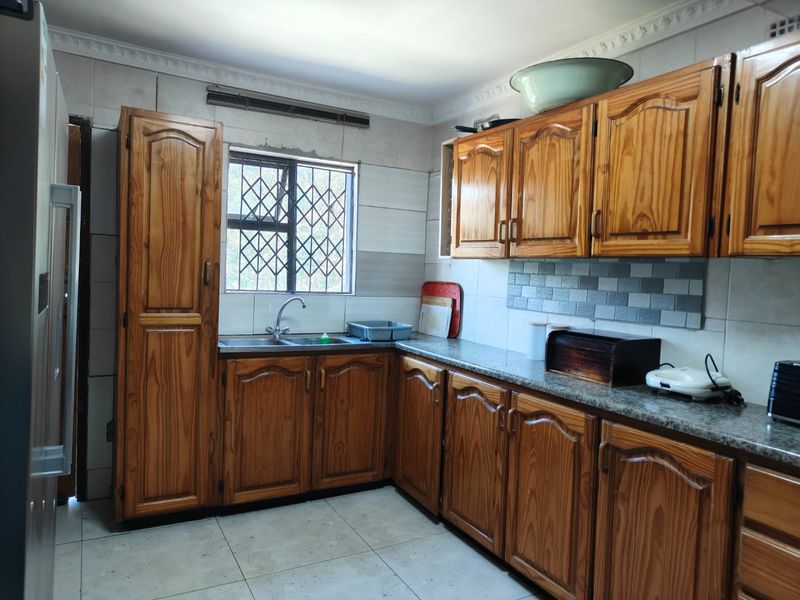 A functional kitchen featuring traditional wooden cabinetry, granite countertops, tiled backsplash, and a window with security bars.