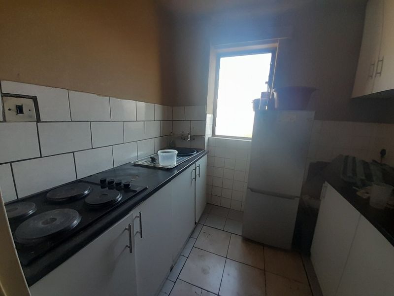 A compact kitchen featuring built-in cabinetry, an electric hob, and a tiled backsplash. The space requires cosmetic updates to improve its overall condition.