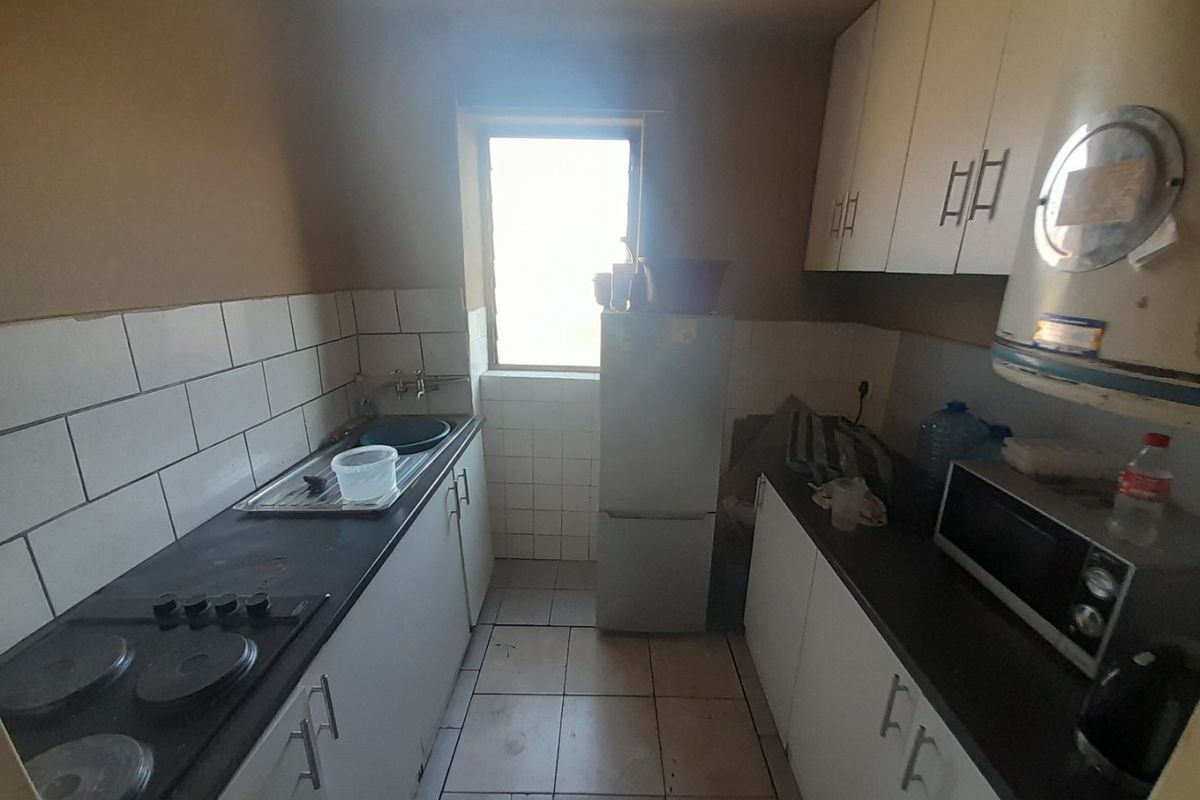 A compact galley-style kitchen featuring built-in cabinetry, a tiled backsplash, and an electric hob, offering a functional layout in need of cosmetic updates.