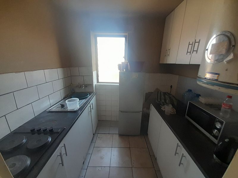 A compact galley-style kitchen featuring built-in cabinetry, a tiled backsplash, and an electric hob, offering a functional layout in need of cosmetic updates.