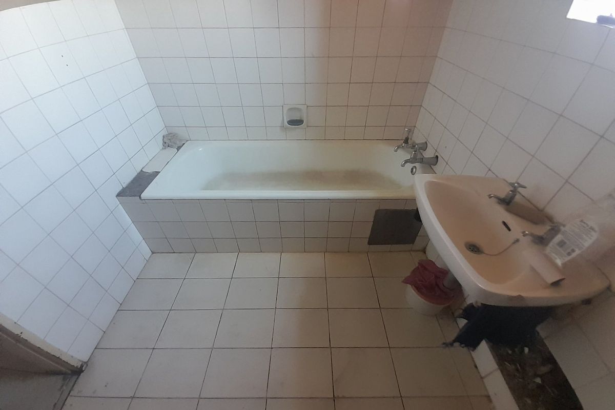 A dated bathroom featuring a built-in bathtub and pedestal basin, requiring significant renovation and repair to the tiling and overall finishes.